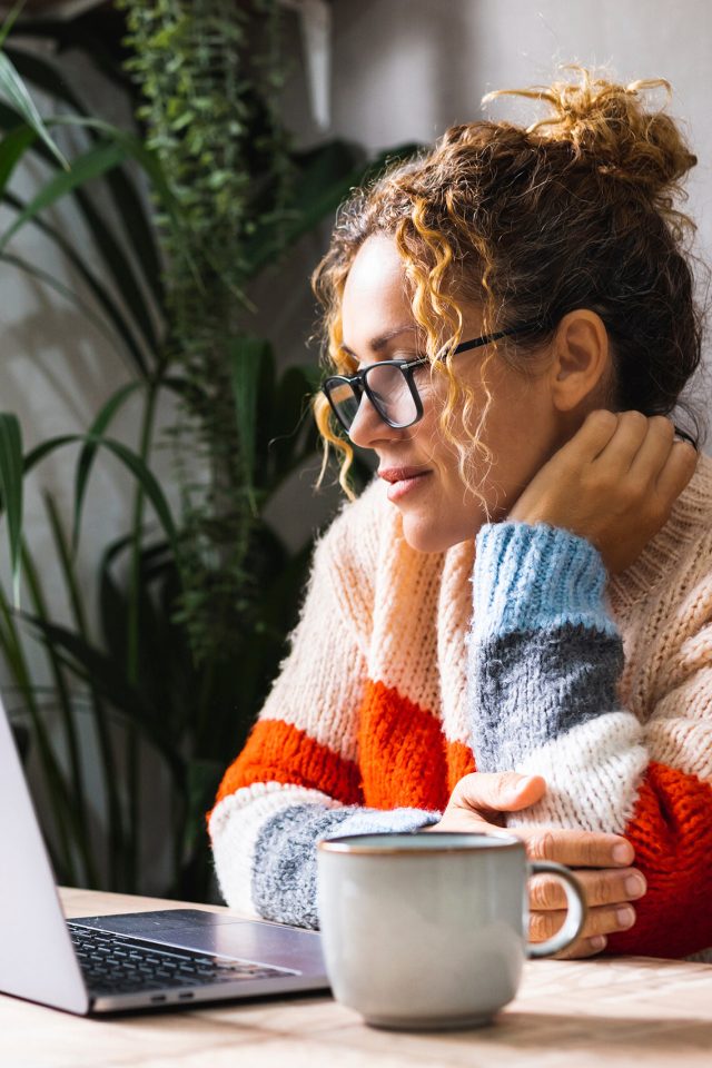 Serene young mature woman looking and reading on laptop online notification email. Pretty female people using computer at home relaxing sitting at the table alone. Modern indoor leisure activity web